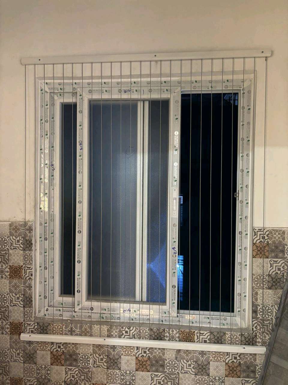 Window fitted with a neat safety grill inside a stone frame by YPL Safety Nets Chennai